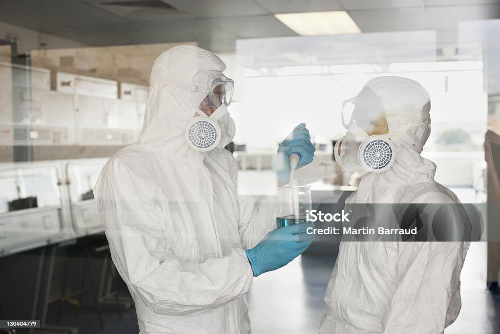 Gli esperti di abbigliamento protettivo mettere il liquido nel becher in laboratorio - Foto stock royalty-free di Tuta protettiva