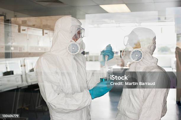 Gli Esperti Di Abbigliamento Protettivo Mettere Il Liquido Nel Becher In Laboratorio - Fotografie stock e altre immagini di Tuta protettiva