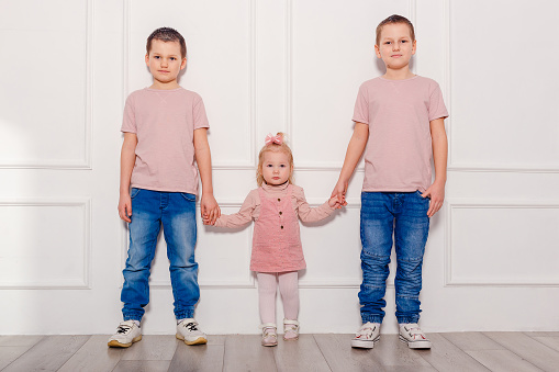 three happy children in pink T-shirts. girl and two boys in full height indoors