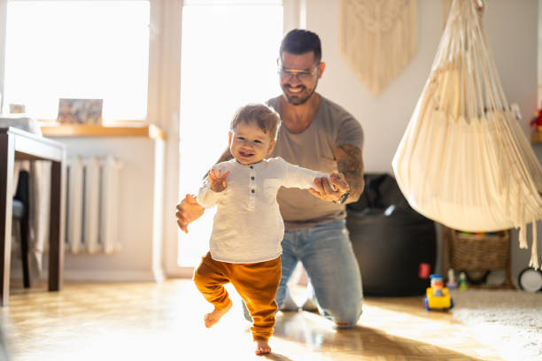 happy father helping little son walking in living room - tattoo father family son imagens e fotografias de stock