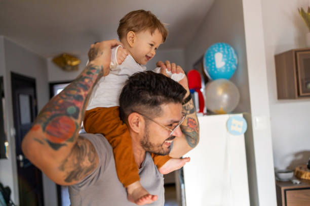 padre felice che porta il figlio sulla spalla mentre si trova a casa - tattoo father family son foto e immagini stock