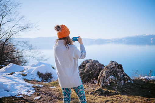 Young woman taking photos of lake with smartphone