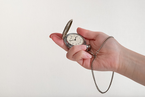 Close-up of human hand holding old pocket watch on light background