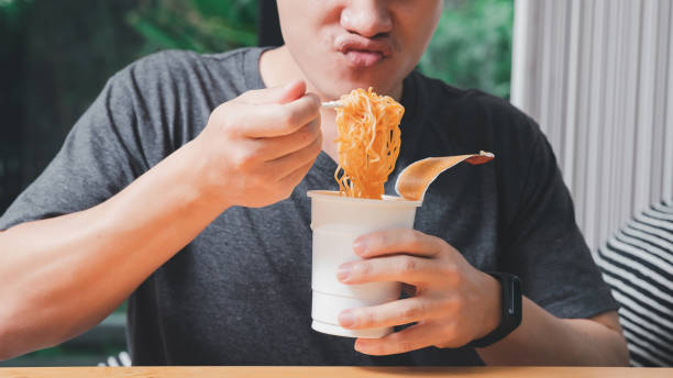 A man holding a plastic fork with cooked instant noodles. Instant noodle is convenient and delicious food.