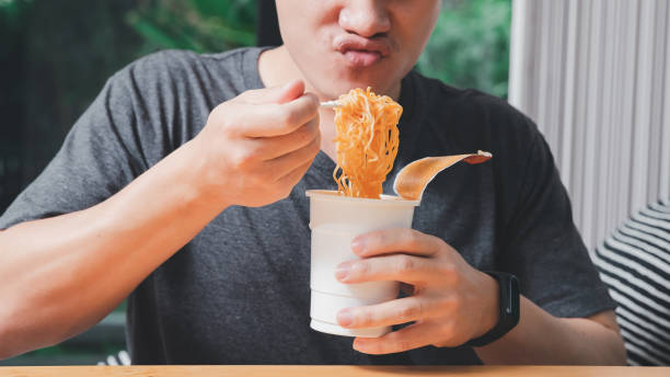 A man holding a plastic fork with cooked instant noodles. Instant noodle is convenient and delicious food. stock photo