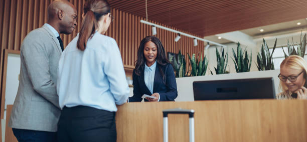 /African American concierge checking in two smiling hotel guests Young African American concierge working behind a reception counter helping two guests check into her hotel concierge photos stock pictures, royalty-free photos & images