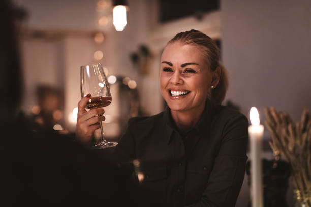Laughing woman talking with a friend at a dinner party Laughing young woman sitting at a table during a candlelit dinner party drinking wine and talking with another guest candle light dinner stock pictures, royalty-free photos & images
