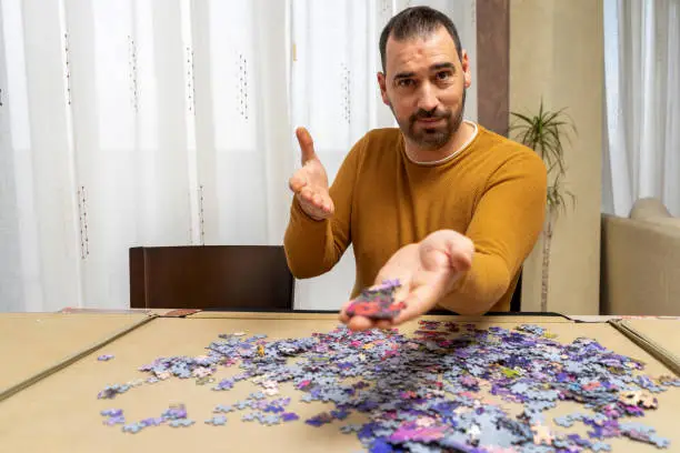 Photo of Handsome bearded man in an orange sweater offering some puzzle pieces with his hands