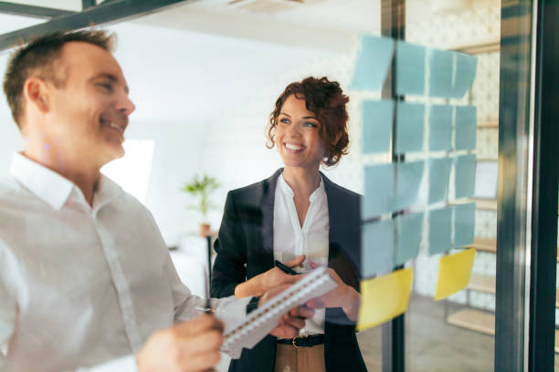 istock Two smiling business people standing near glass wall with post it notes, portrait. 1304061684
