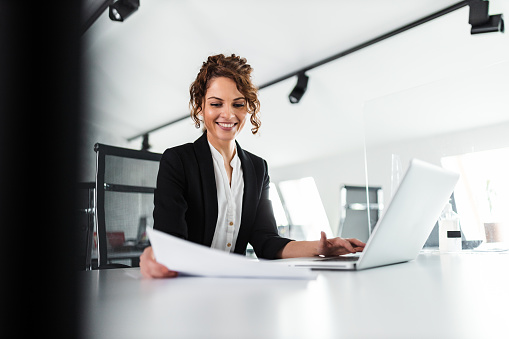 Portrait of a happy businesswoman looking at paper document and smiling. Business success concept.