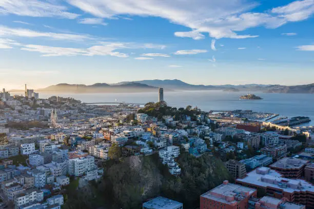 Aerial view of Coit Tower and Russian Hill as the sun begins to set. Alcatraz is visible in the Bay and the Golden Gate bridge in the distance.