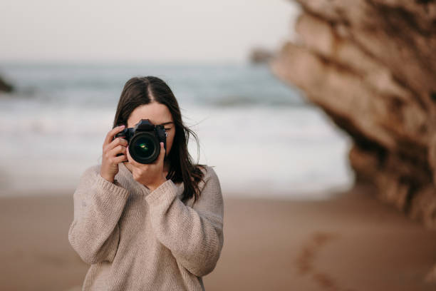 istock Young woman at beach taking a picture with a DSLR camera 1304065598