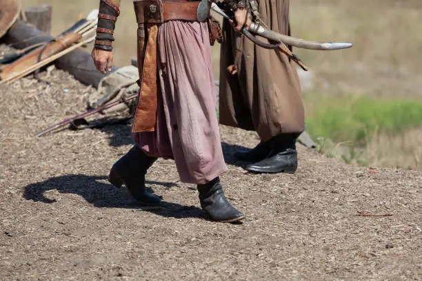 Vintage Cossack warrior in leather boots and wide pants holds a wooden bow and arrow in his hands