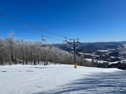 A triple chair lift at Plattekill Mountain on a sunny day with lots of snow, no people on the chair lift