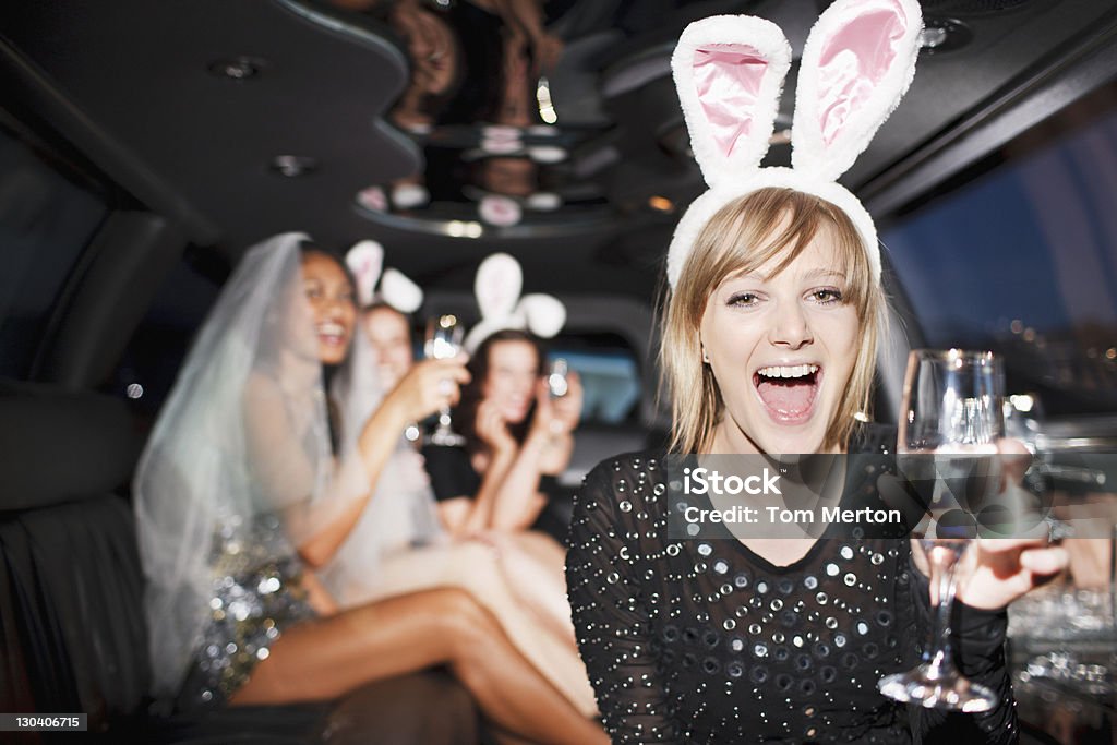 Woman in bunny ears drinking champagne in limo  Bachelorette Party Stock Photo