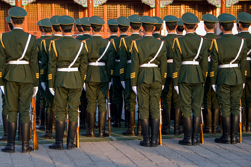Unrecognizable group of Chinese soldiers standing in line and seen from behind. Wearing uniforms including caps. The soldiers belong to the Chinese armed forces.