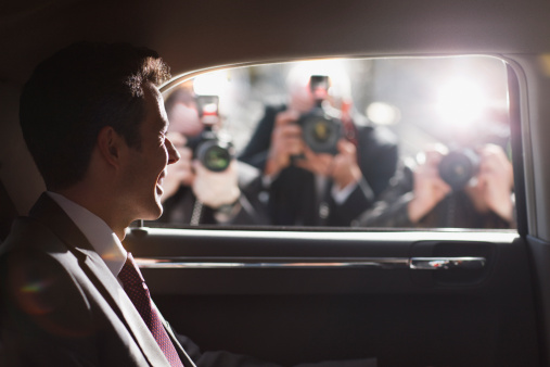 Politician smiling for paparazzi in backseat of car