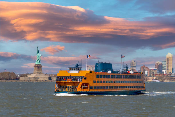 Staten Island ferry coming from Manhattan and passing by the Statue of Liberty. The Statue of Liberty and the skyscrapers of lower manhattan can be seen in the background.