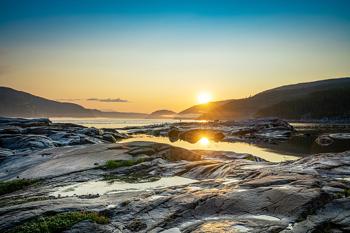 Sunset over the fjords in Tadoussac, Quebec, Canada, at low tide with rocks in foreground