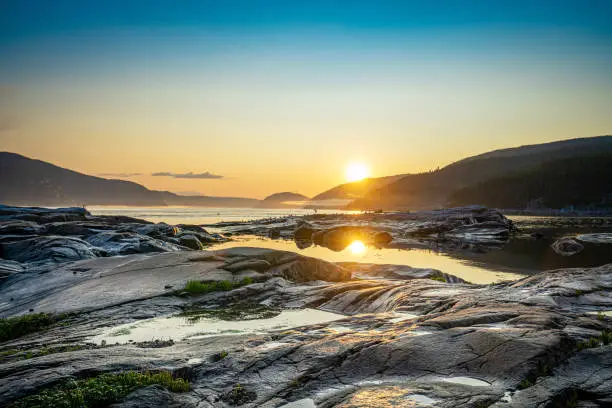 Photo of Sunset over the fjords in Tadoussac, Quebec, Canada, at low tide with rocks in foreground