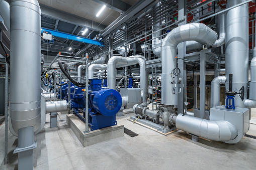 Huge industrial boiler services and air handling unit in the ventilation plant room with ductworks and insulated pipelines