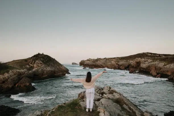 Photo of Young woman with arms raised by the sea