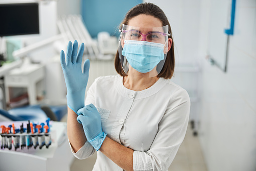 Woman smiling under the facial mask while getting her right hand into an elastic hospital glove