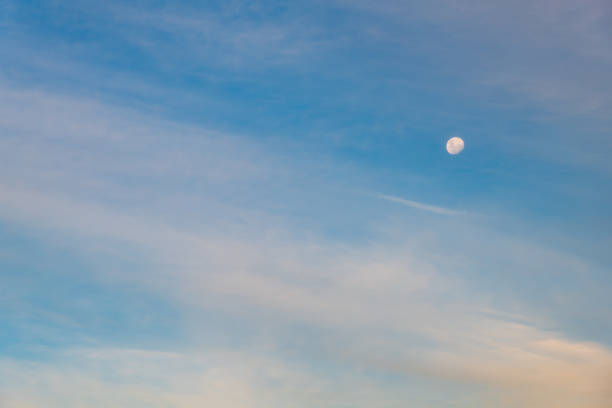 Beautiful blue sky with clouds and half moon at sunset.