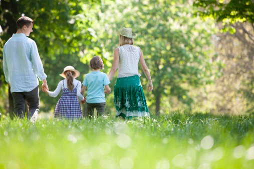 Young couple, man and woman going for a walk in park with their little children, boy and girl, playing on warm summer day outdoors. Concept of family, childhood and parenthood, fun, weekends, love, ad