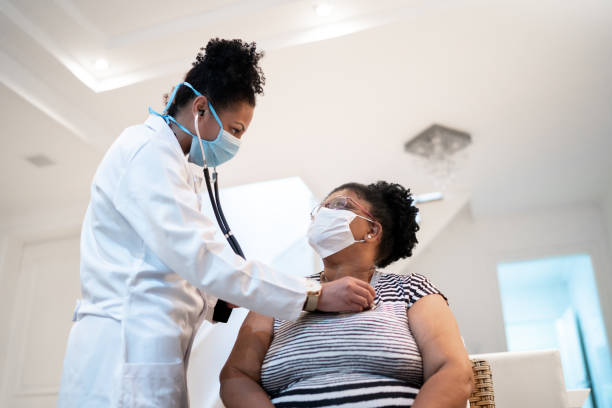 doctor listening to patient's heartbeat during home visit - wearing face mask - doctor stethoscope healthcare worker professional occupation imagens e fotografias de stock