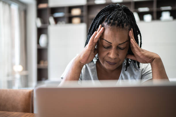 mujer madura con dolor de cabeza frente a portátil en casa - financial burden fotografías e imágenes de stock