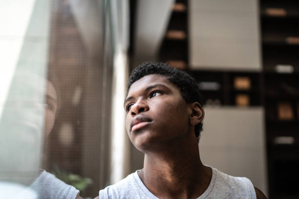 teenager junge schaut durch das fenster zu hause - pensive stock-fotos und bilder