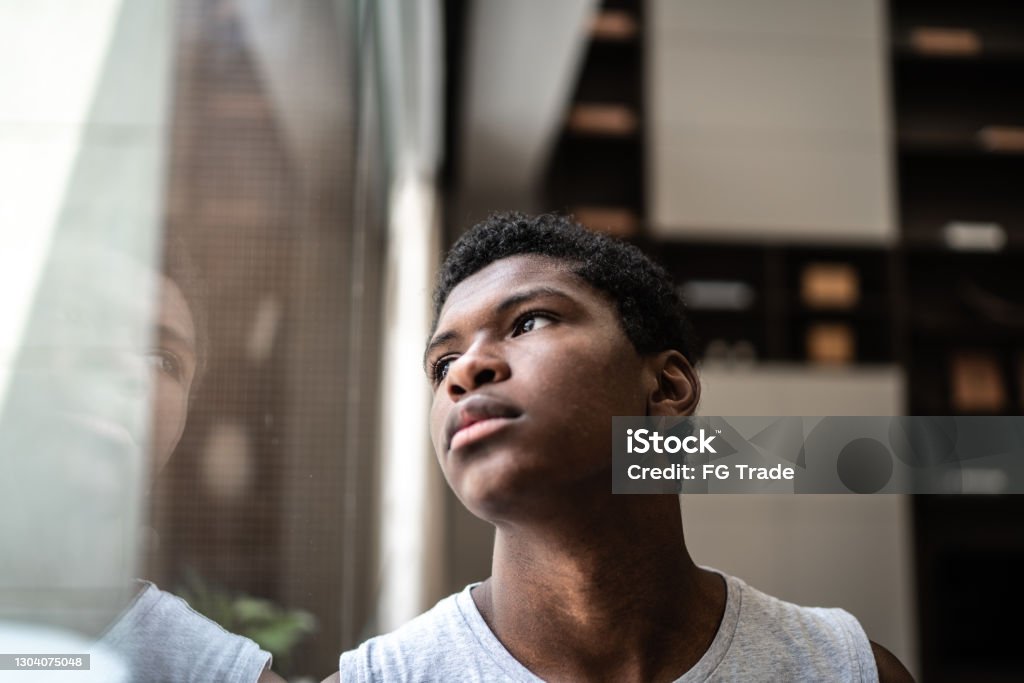 Teenager boy looking through the window at home Teenager Stock Photo