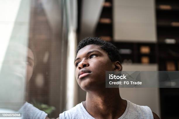 Teenager Boy Looking Through The Window At Home Stock Photo - Download Image Now - Teenager, Sadness, Teenage Boys