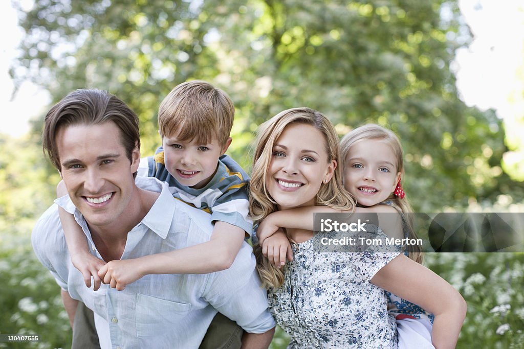 Genitori con i loro figli piggyback all'aperto - Foto stock royalty-free di Famiglia