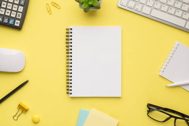 istock Photo overhead of notebook keyboard calculator pen computer mouse notes plant glasses and paperclips isolated bright color yellow backdrop 1304076596