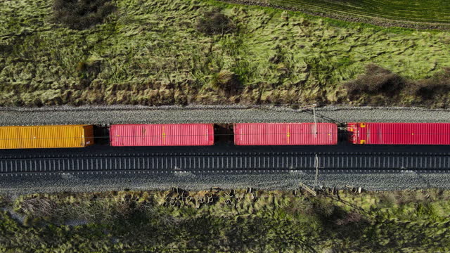 Aerial top view of the freight train, carrying colorful containers, moving through the forest at sunset. 4K footage from drone. High quality 4k footage