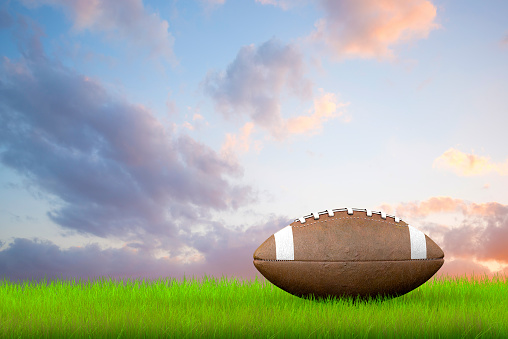 American Football Ball Ball in green field and behind cloudy sky