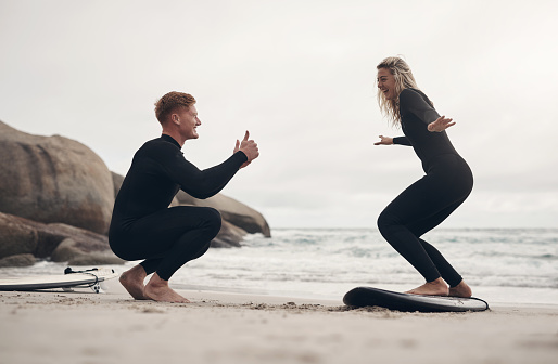Shot of a man giving a woman surfing lessons on the beach