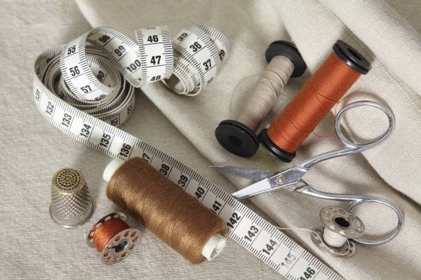 istock sewing tools with scissors, brown threads, needle and tape measure. Dressmakers accessories on beige fabrics 1304082484