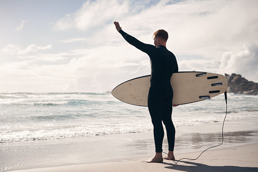 Shot of a young man holding his surfboard while at the beach