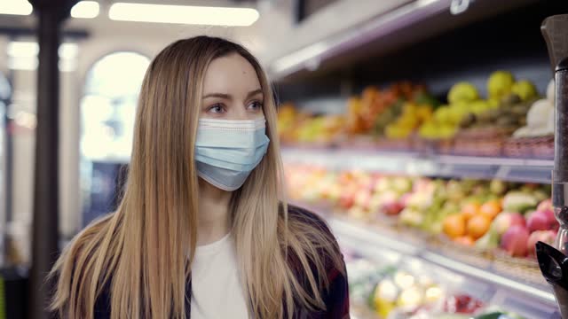 Woman in protective mask looking for fruits in supermarket