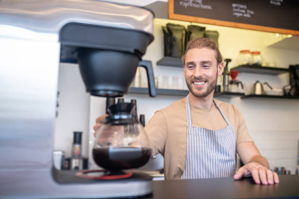 istock Smiling man with coffeepot near coffee maker behind counter 1304084036
