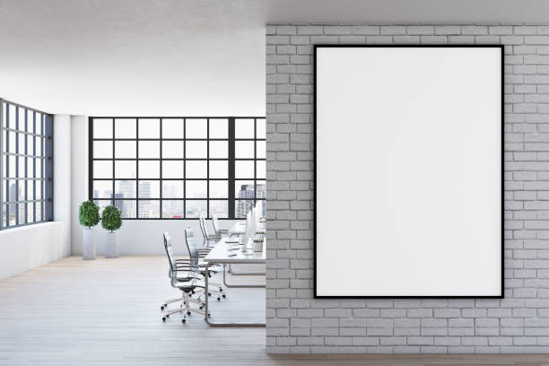 istock Blank white poster in black frame on light brick wall in spacious modern office with wooden floor and big window. Mock up 1304087207