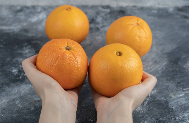 istock Female hand holding oranges on marble background 1304094481