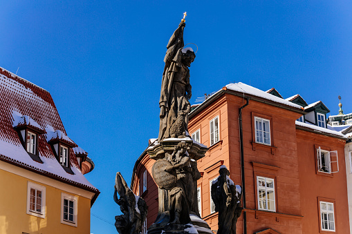 Baroque sculpture of St. John the Baptist with angels at Maltese Square, sunny winter day, snow on red roofs, Mala Strana or Lesser Town district, Prague, Czech Republic, February 14, 2021