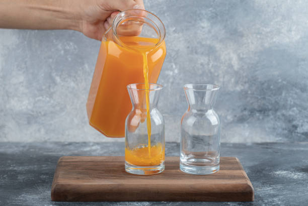 istock Man hand pouring orange juice into glass on marble background 1304102952