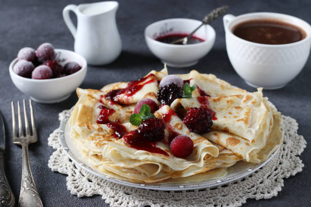 istock Thin pancakes with wheat flour, eggs and kefir, served with berries, jam and cup of cofee on gray table. Closeup 1304103758