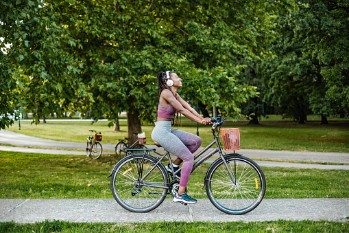 Photo of a young African American woman is on her bicycle using wireless headphones