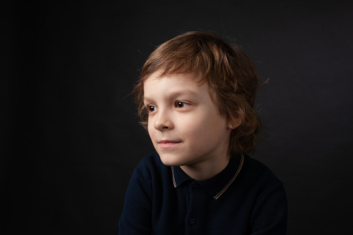 Close up studio portrait of 7 year old boy with long brown hair in polo shirt on black background